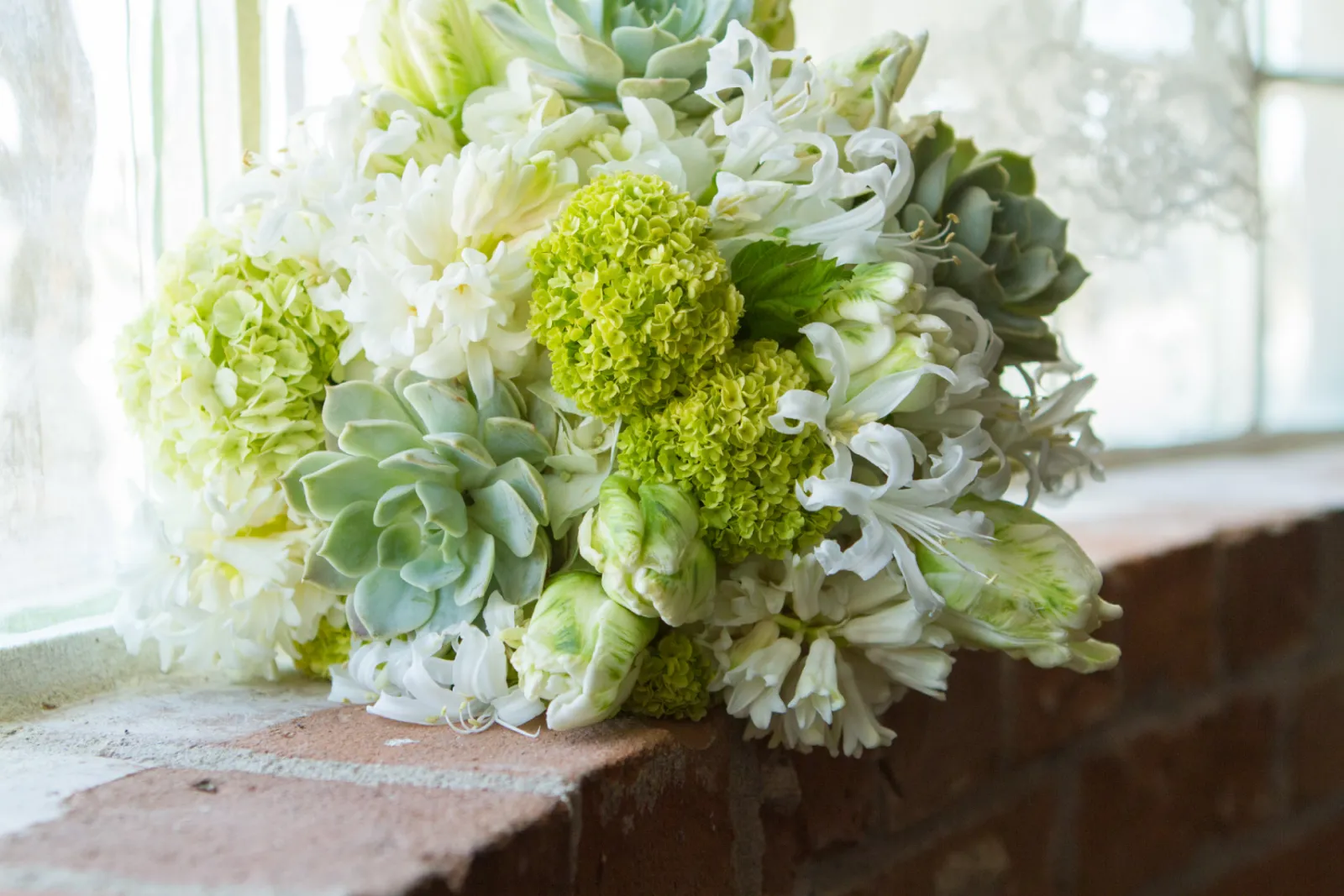 White tulips, green hydrangea, succulents, and agapanthus bouquet resting on a brick windowsill