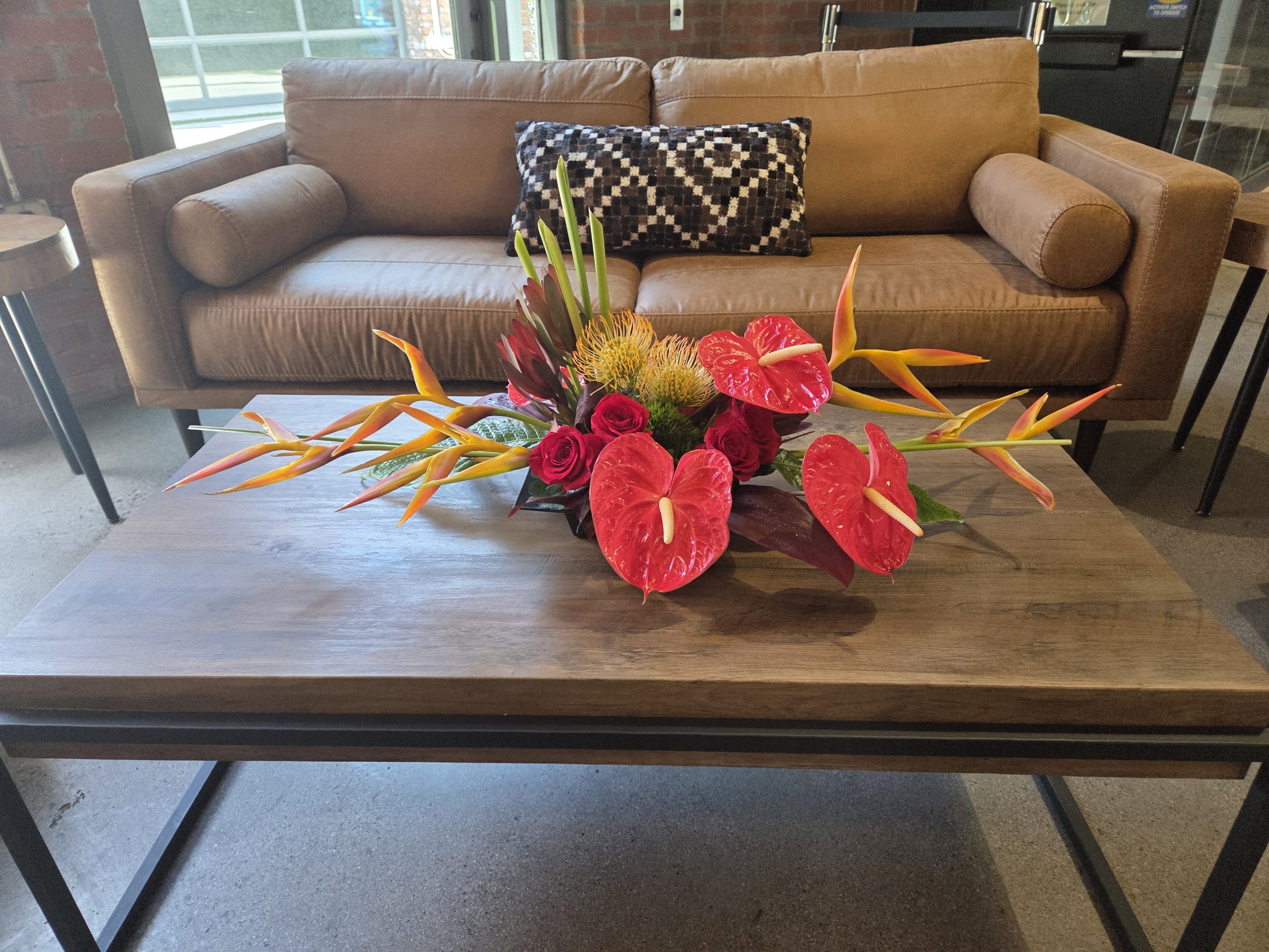 Tropical flowers arrangement with red roses, anthurium, and heliconia on coffee table