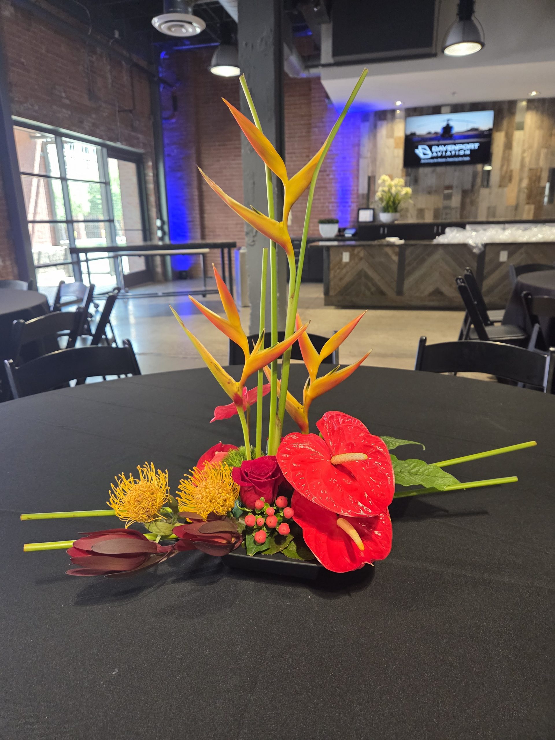Tall tropical flowers arrangement with heliconia, red anthurium, and protea for event centerpiece